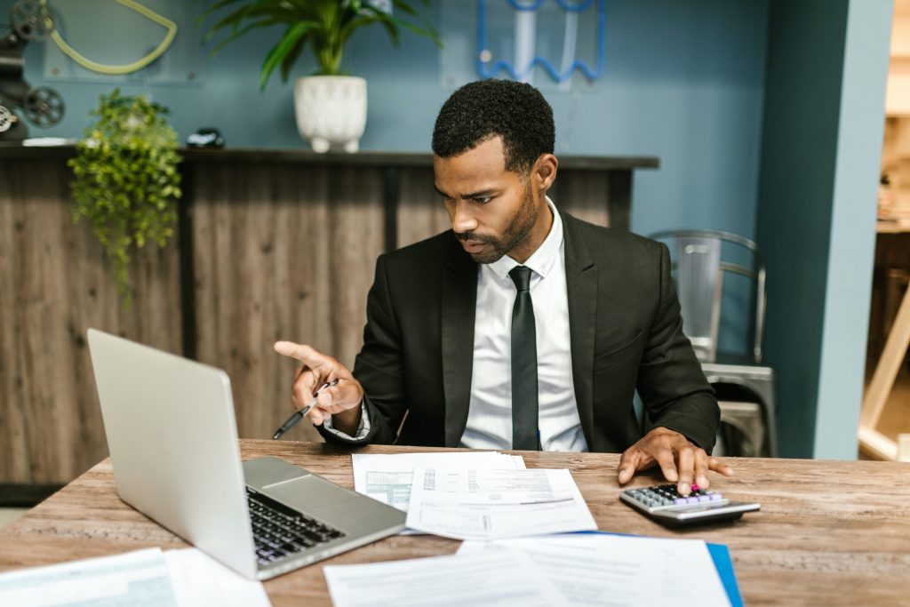 Man at desk with calculator and papers pointing to laptop screen. Calculating the cost of downtime and cyber liability insurance.